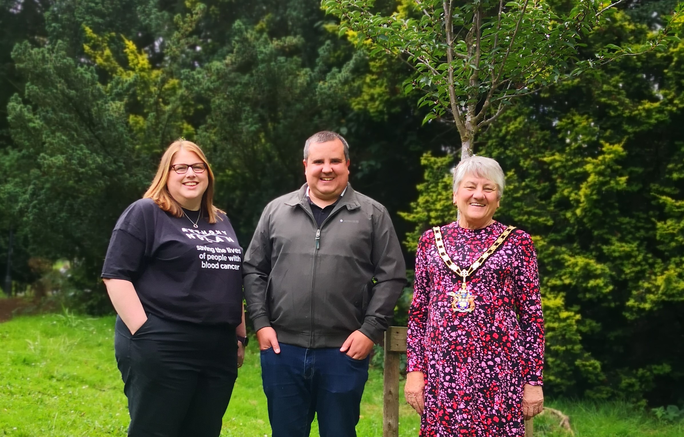 A group of three people stood in front of a young tree in Arnot Hill Park, Arnold. One of the group is wearing a t-shirt reading 